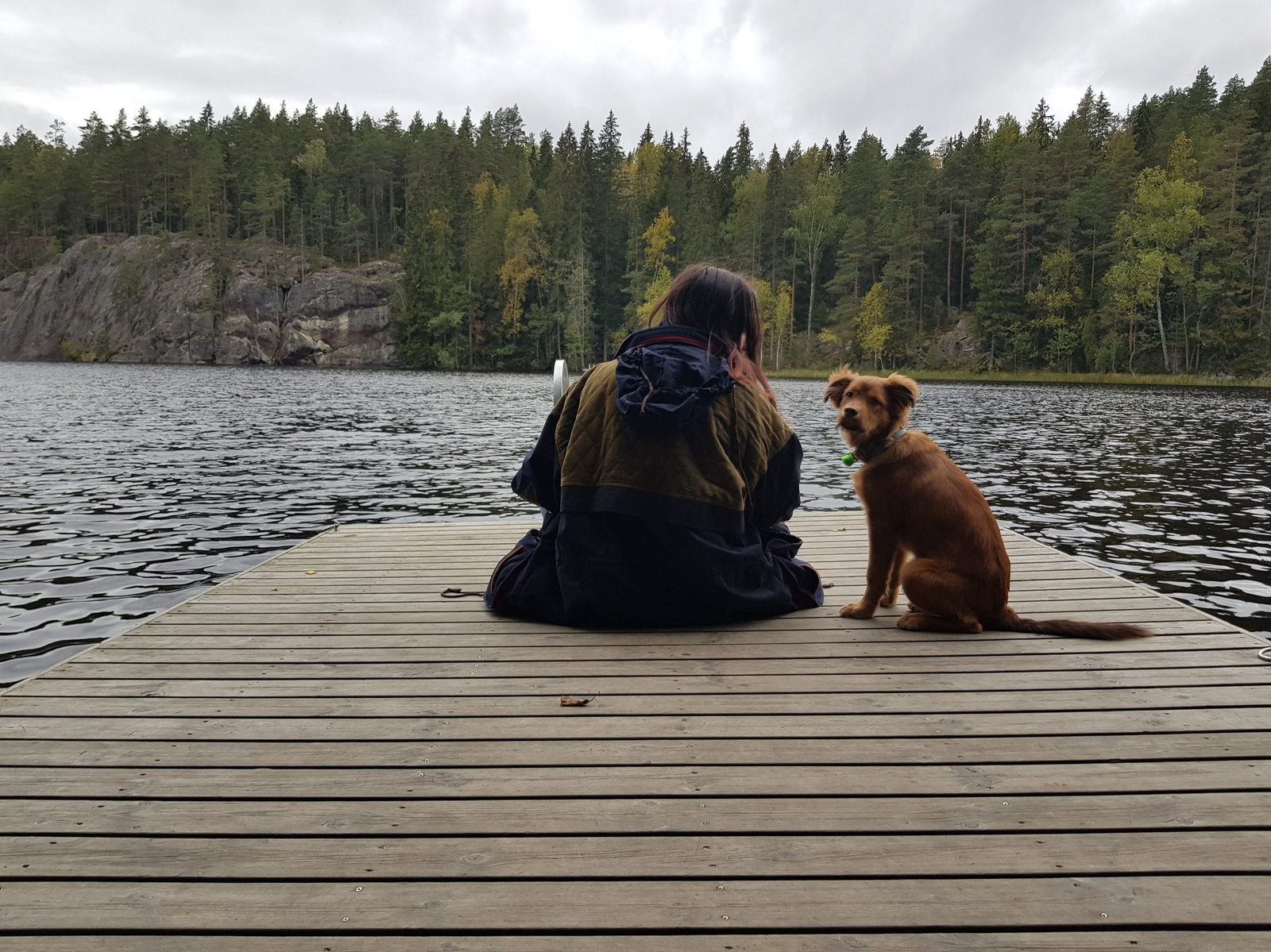 Ángela y Kobe de espaldas, sentados en un muelle junto al lago